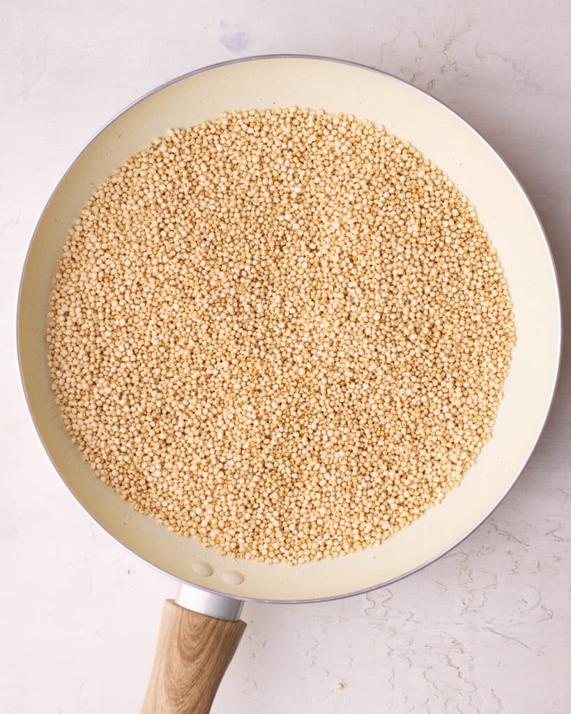 Quinoa being toasted in a dry frying pan.