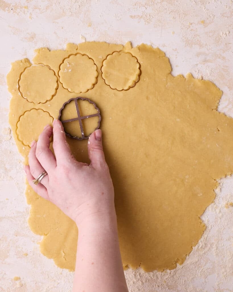 Rolled out shortbread cookie dough being cut into circular shapes with a flute-edged cookie cutter.