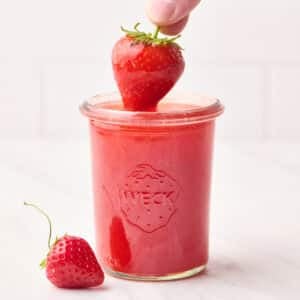 Strawberry glaze in a mason jar with a strawberry being dipped in it.