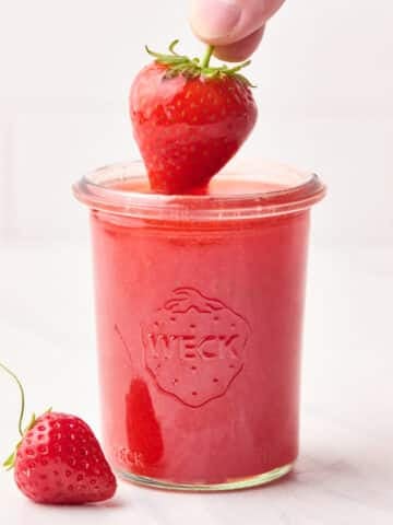 Strawberry glaze in a mason jar with a strawberry being dipped in it.