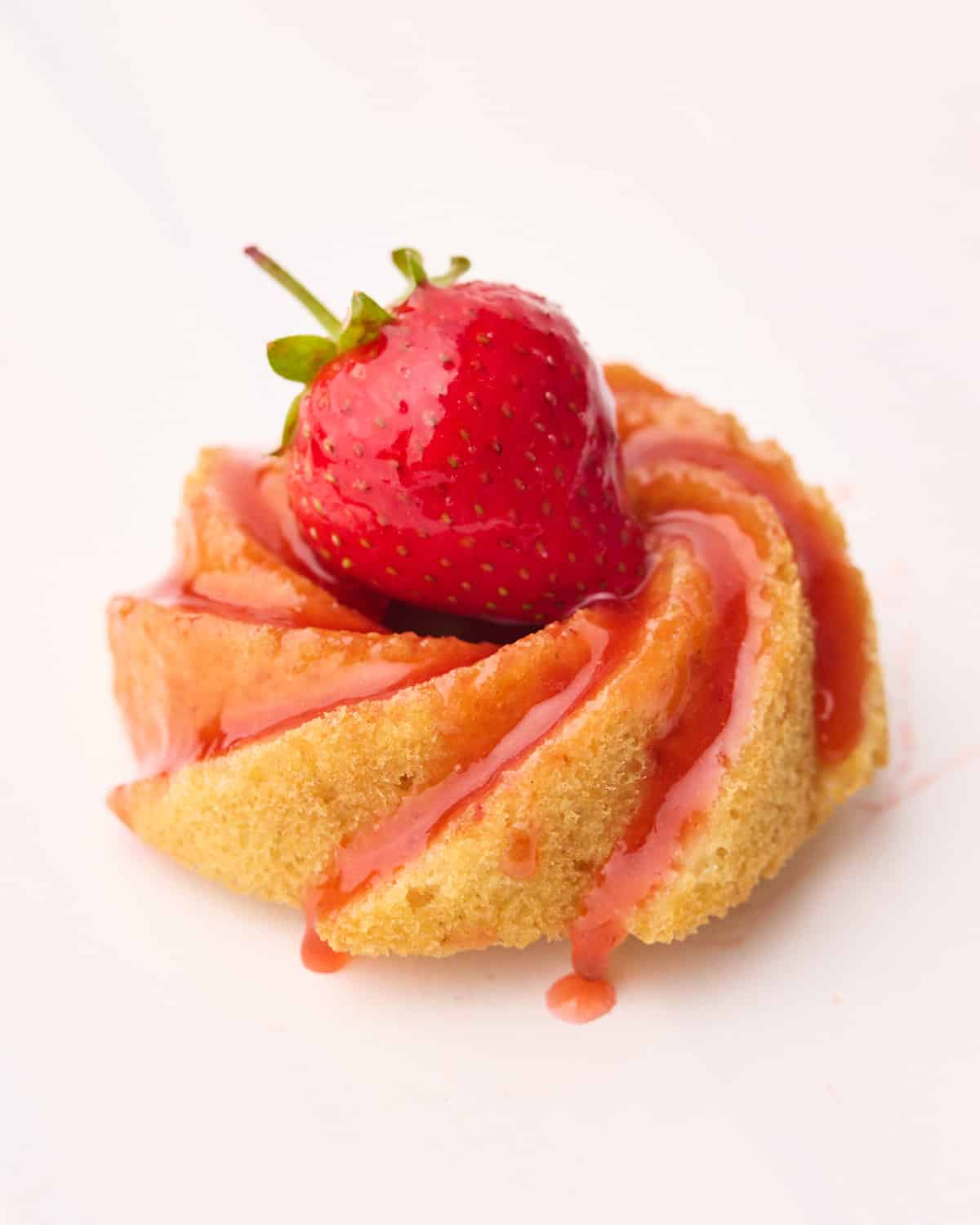 Mini bundt cake covered in strawberry glaze and a fresh strawberry on top.