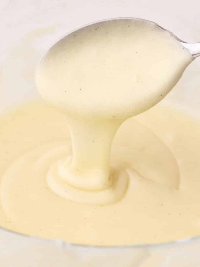 Powdered sugar vanilla glaze in a glass bowl, being drizzled off of a spoon.
