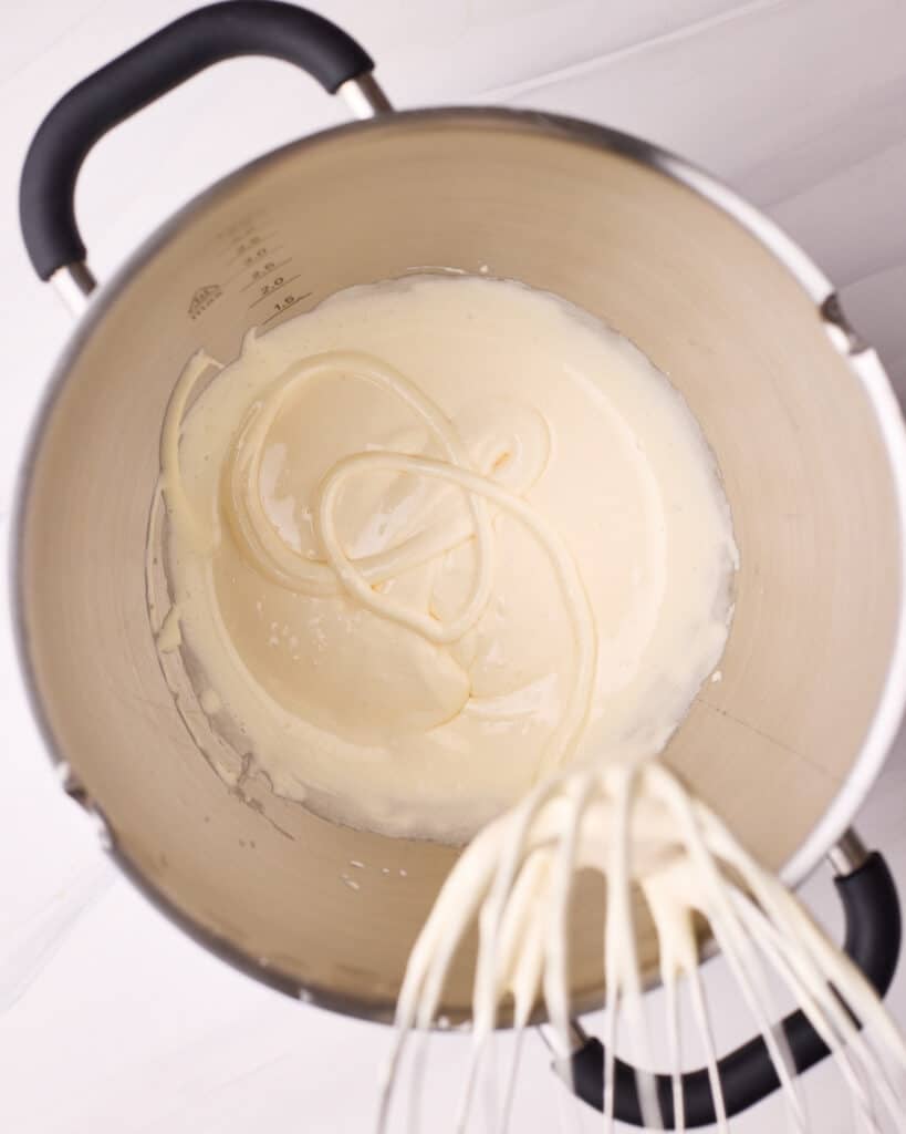 Whisking eggs and sugar together in a bowl until they are pale and thick and leave a trail behind on the surface.