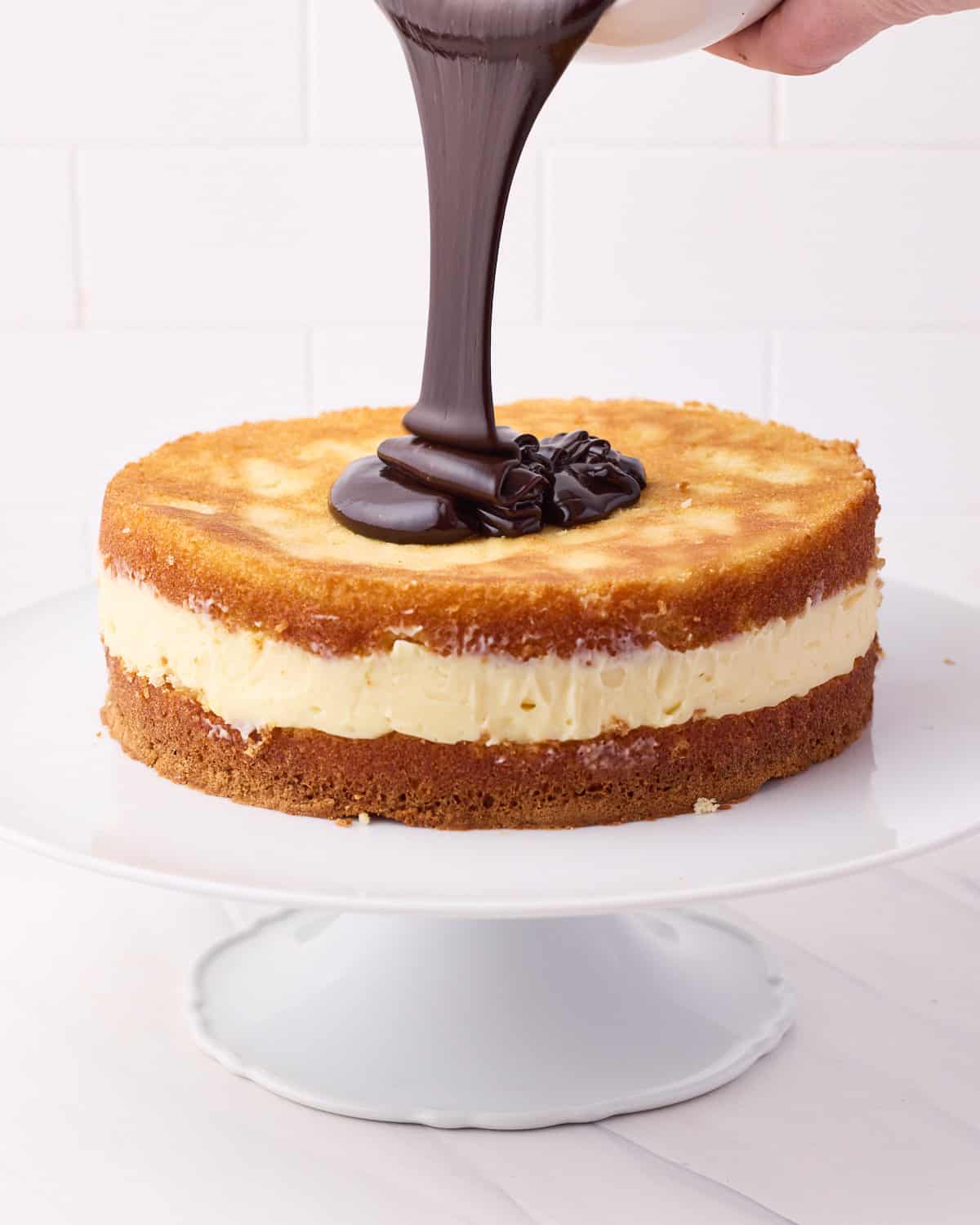 Chocolate glaze being poured over Boston Cream Pie.