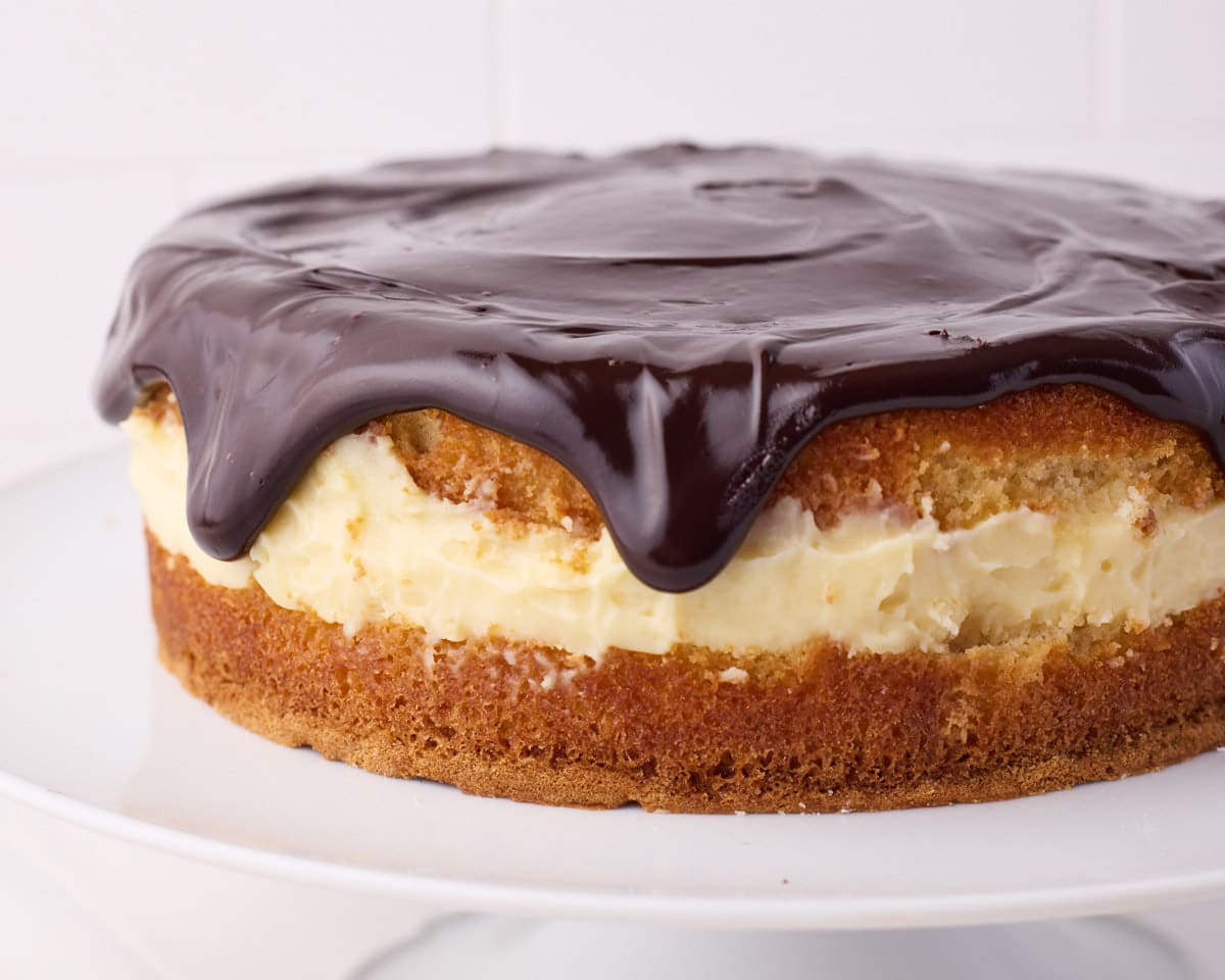 Boston cream pie from the side to show the layers of sponge cake, pastry cream filling and shiny chocolate glaze.