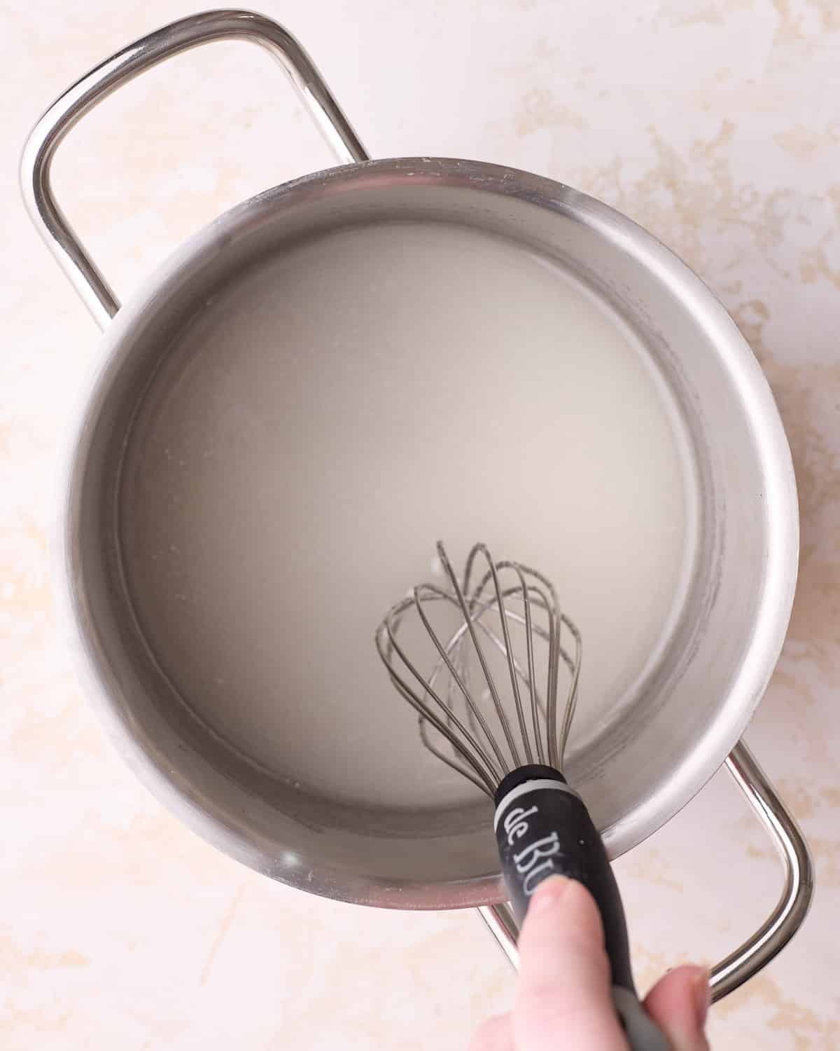 Combining sugar and water in a saucepan to make a sugar syrup.