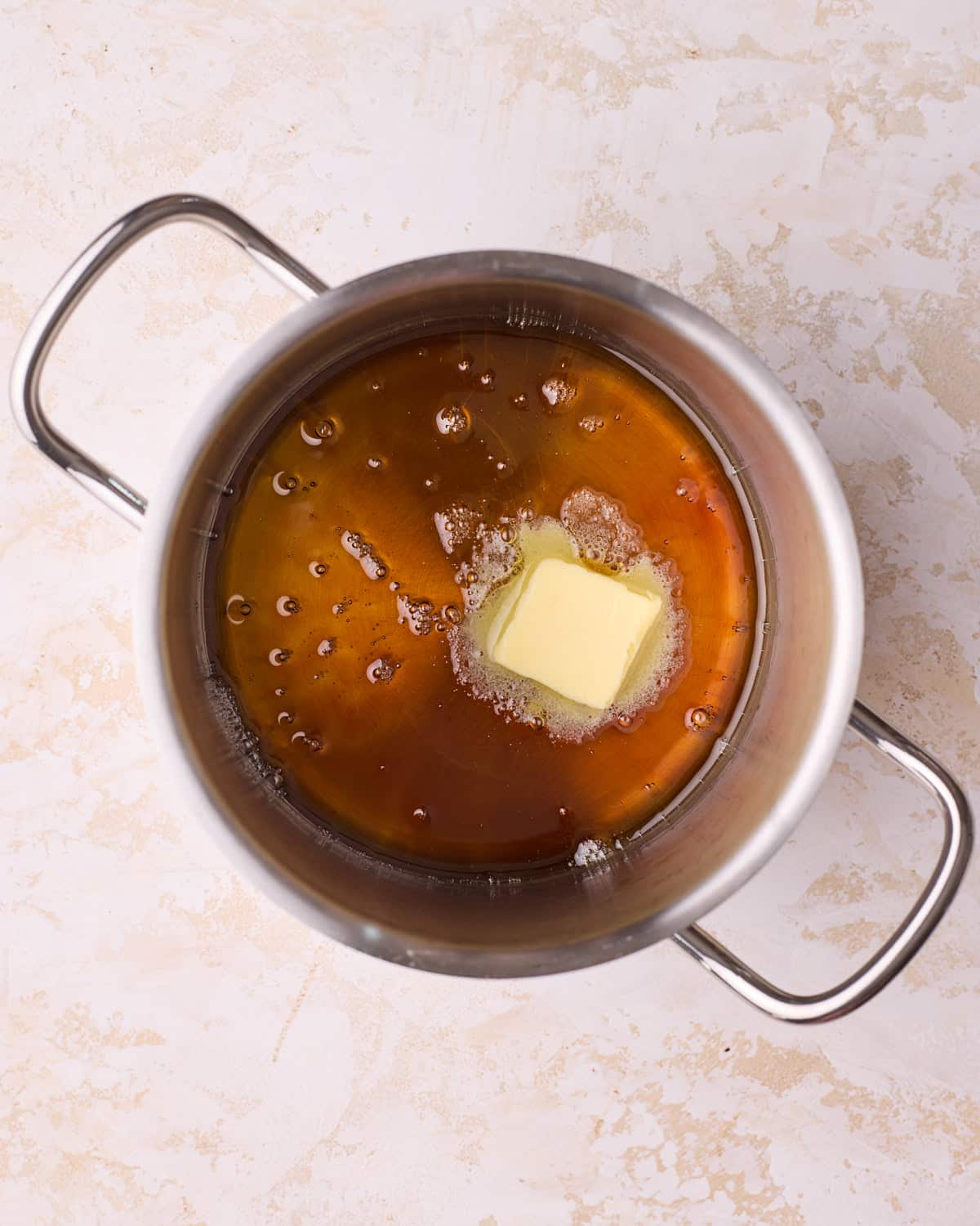 Adding a chunk of butter to homemade caramel sauce, it is fizzing up slightly at the edges.