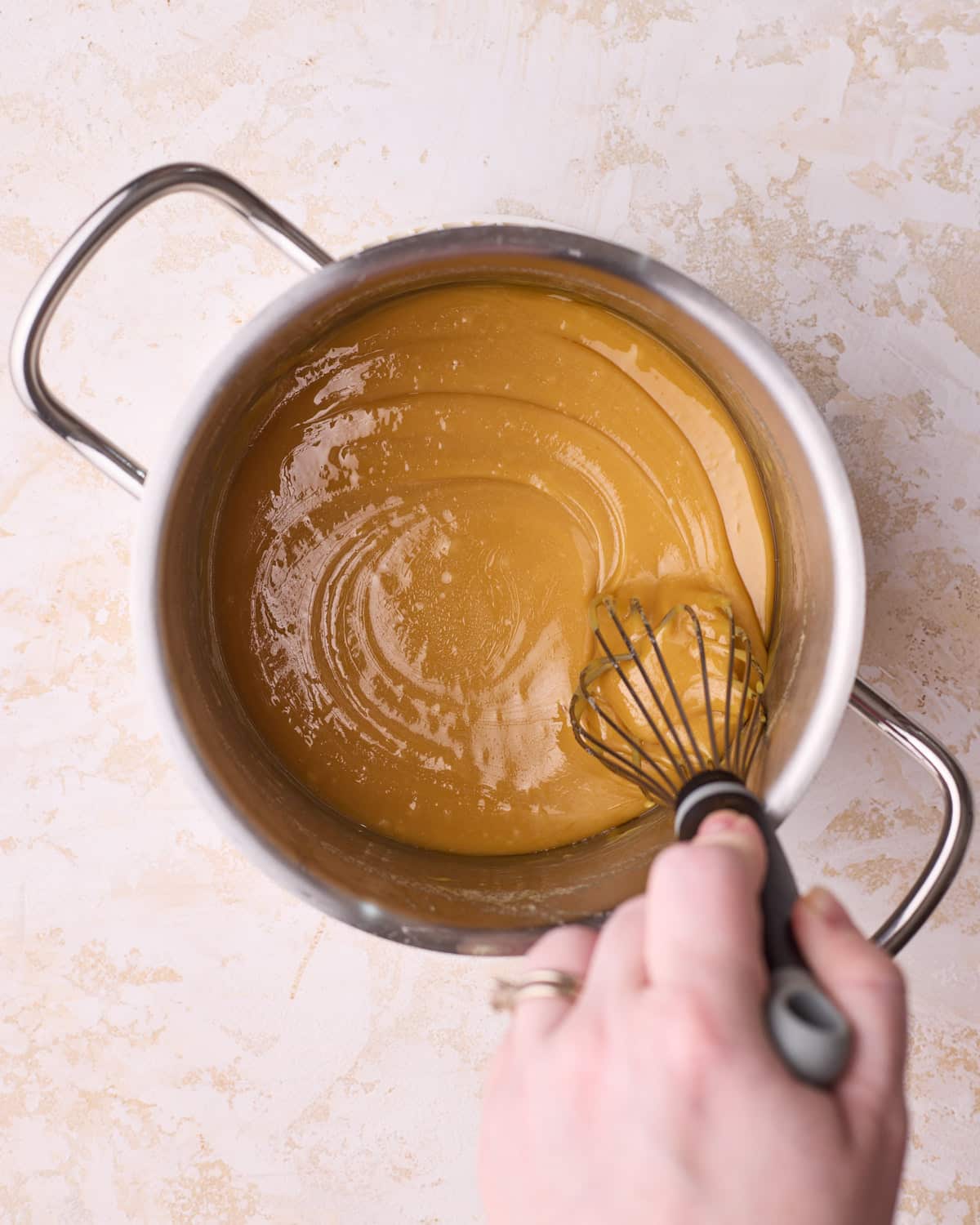 Whisking homemade caramel in a stainless steel pan.