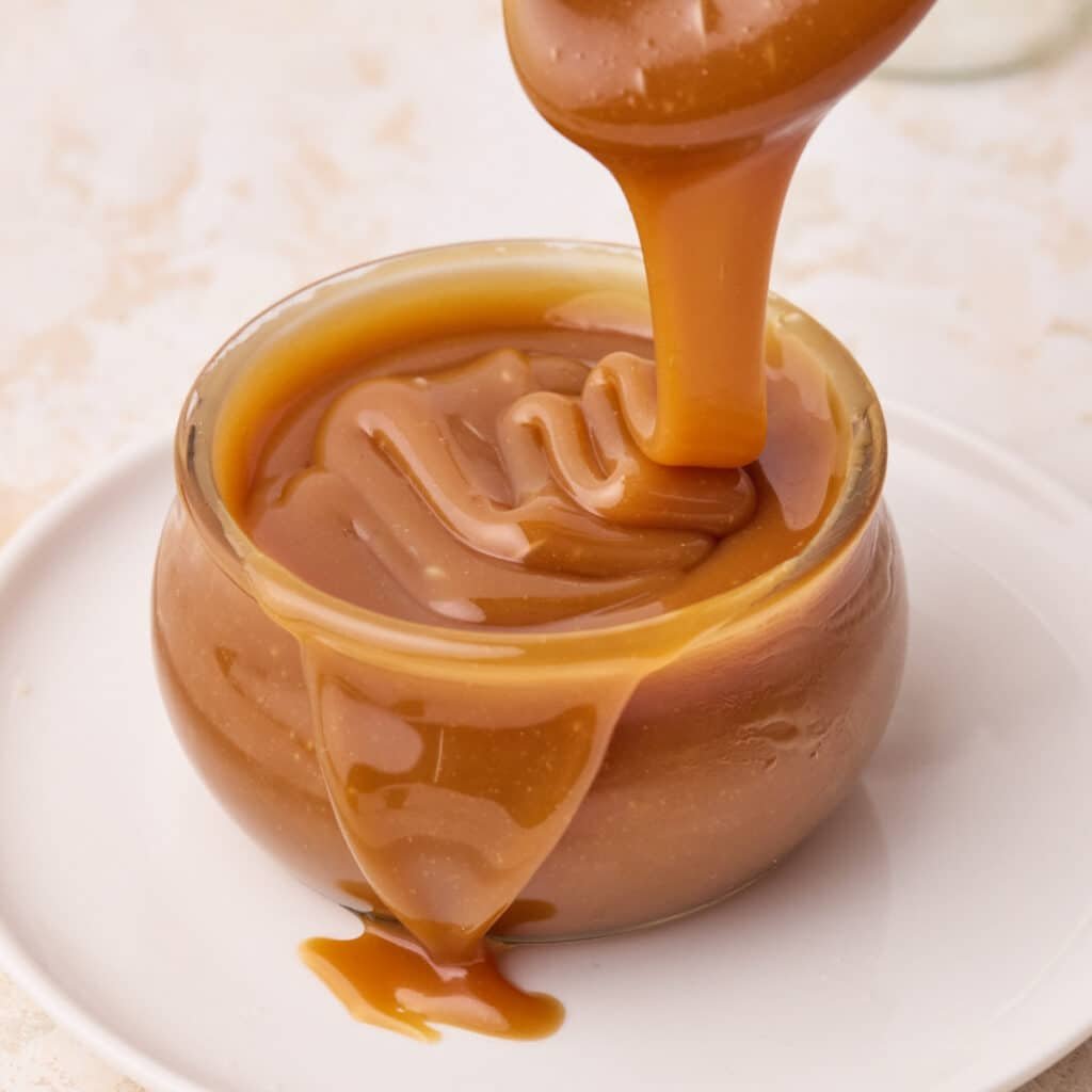 Homemade caramel sauce being poured into a glass jar.