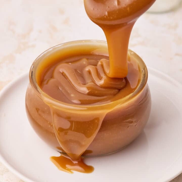 Homemade caramel sauce being poured into a glass jar.
