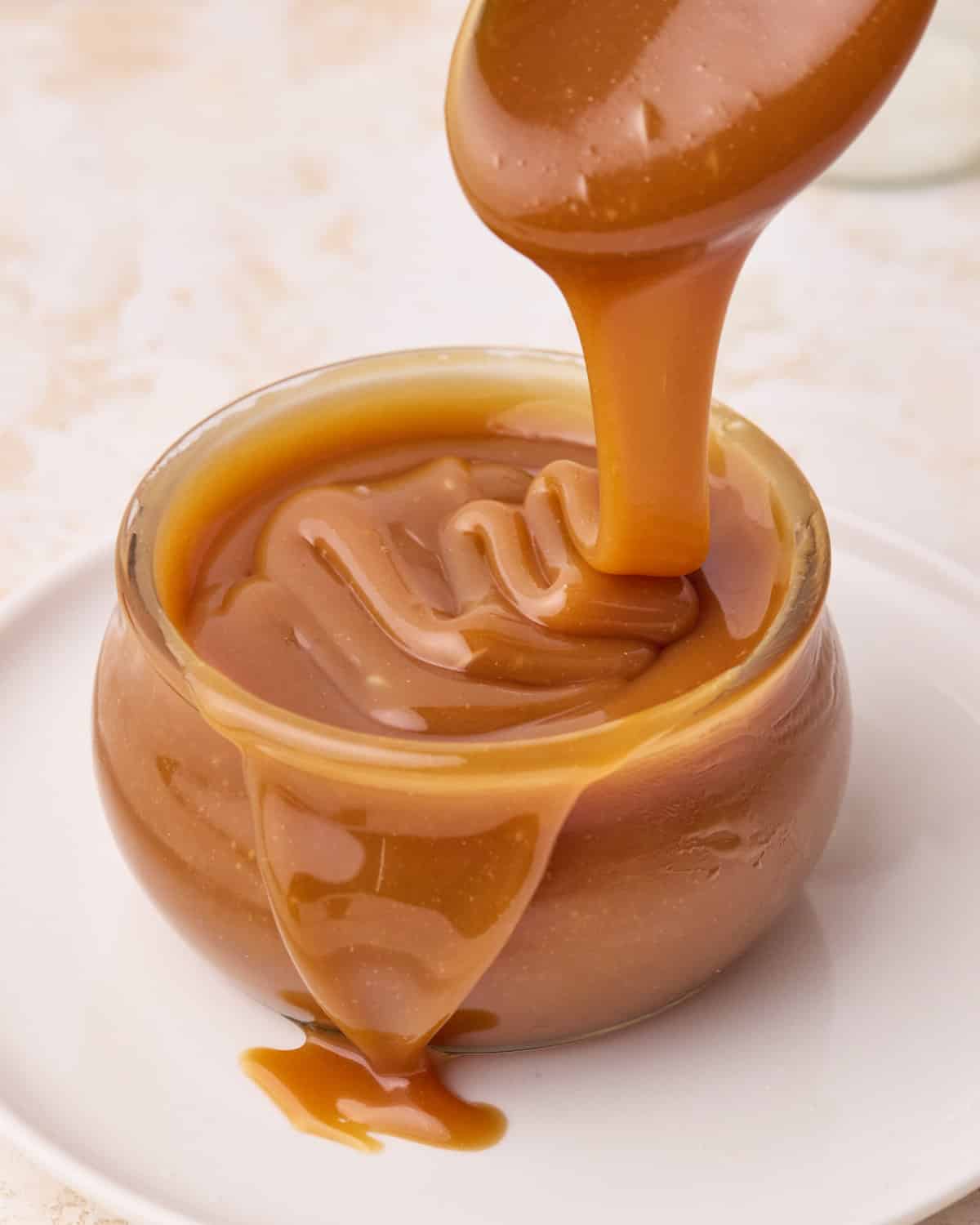 Homemade caramel sauce being poured into a glass jar.