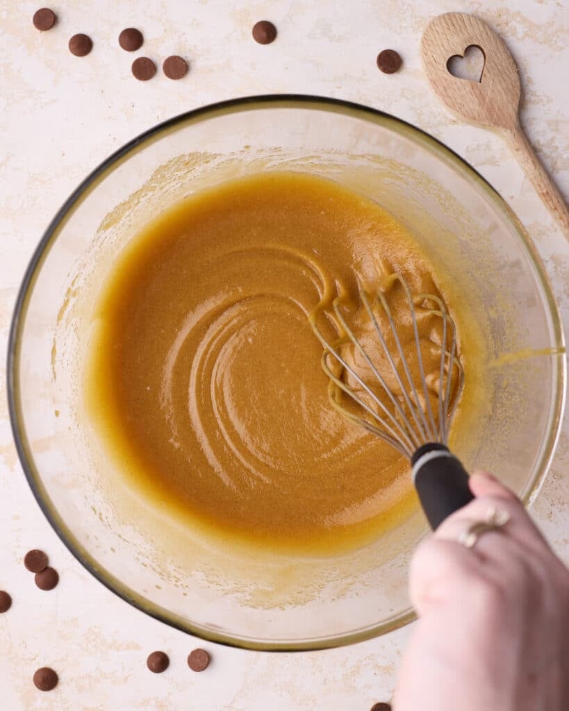 Wet ingredients being whisked into the sugar and butter mixture, including egg, egg yolk, and vanilla.