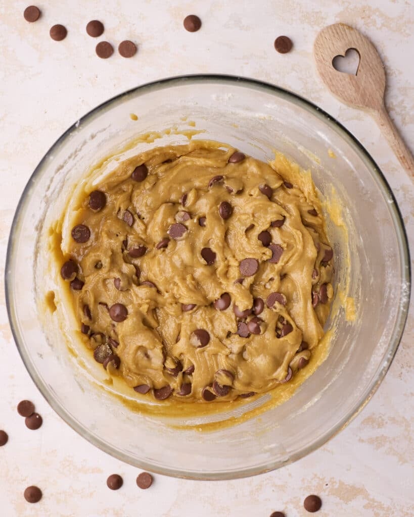 Chocolate chip cookies dispersed into the cookie dough mixture in a bowl.