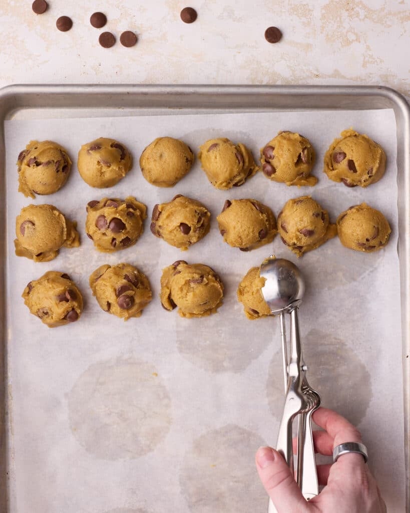 Little cookie dough balls being placed next to each other on a baking sheet using a cookie scoop.