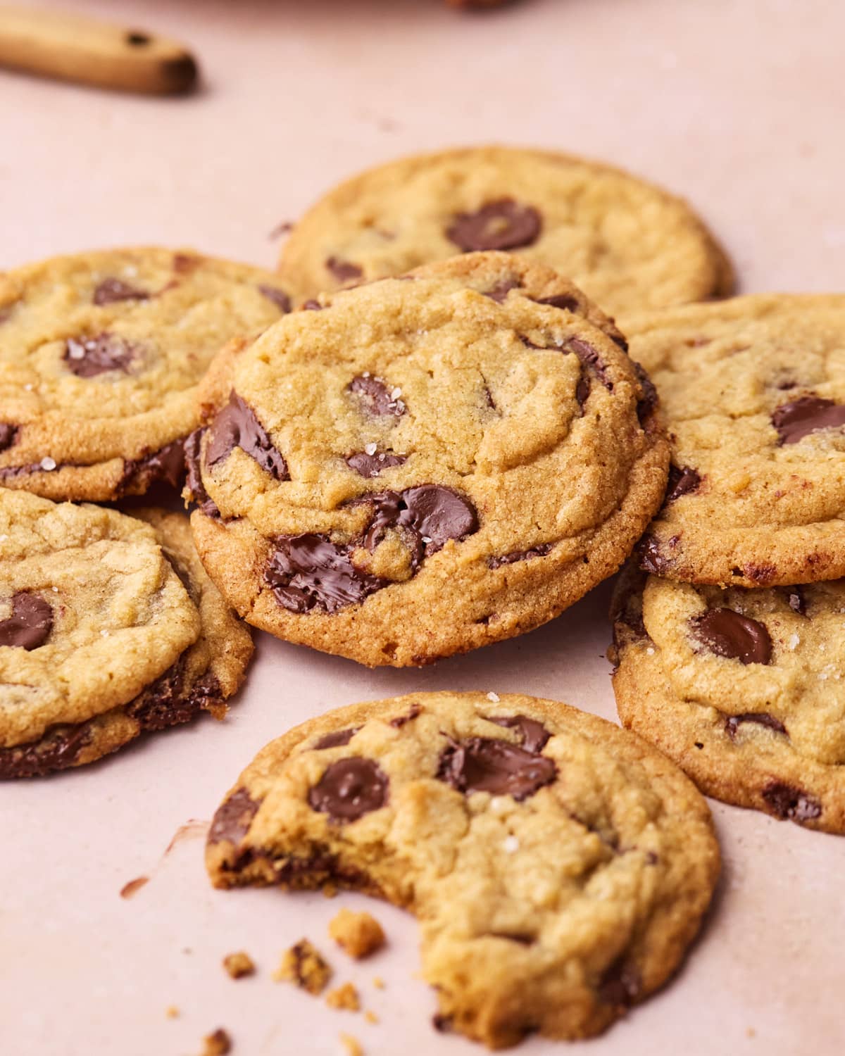 A bundle of chocolate chip cookies lying on top of each other, one with a bite taken out of it. 