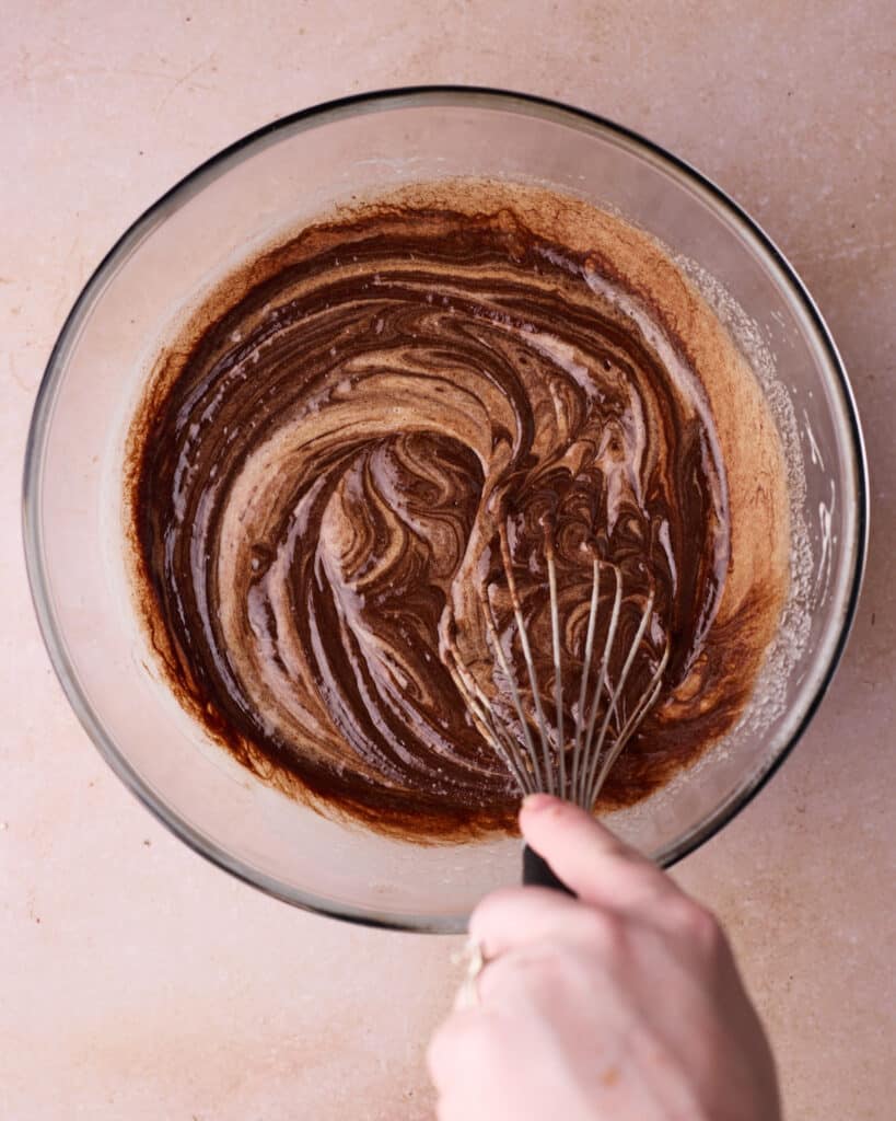 Mixing together the melted chocolate and egg mixture in a bowl with a whisk.
