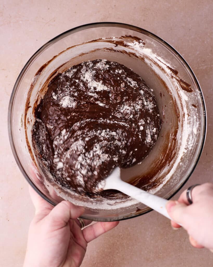Flour being folded into the chocolate batter with a rubber spatula.