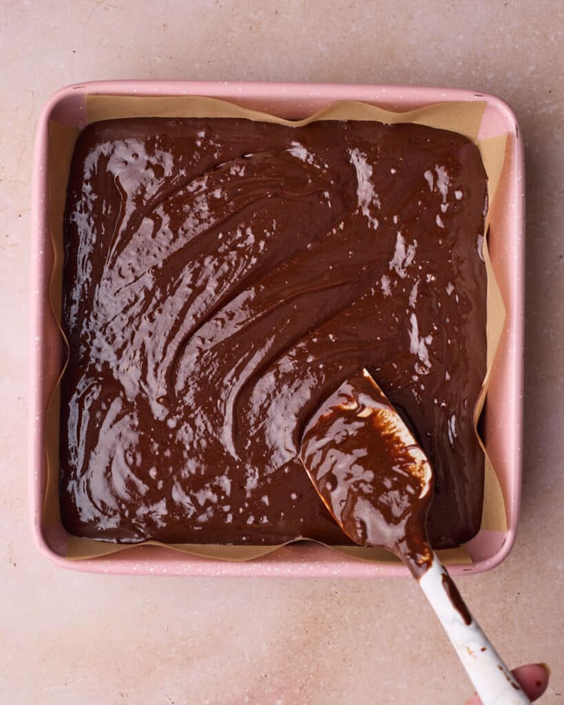 Fudgy brownie batter being smoothed out into a square pan.