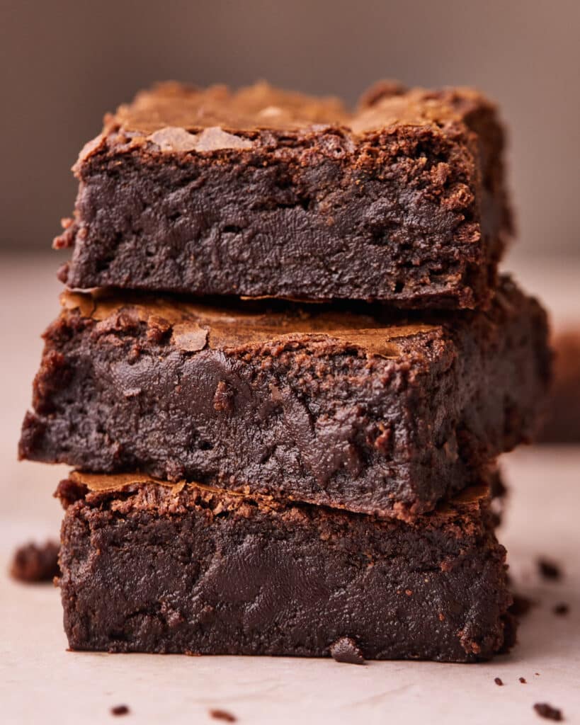 Side view of 3 thick fudgy brownies stacked on top of each other, showing off the gooey texture.