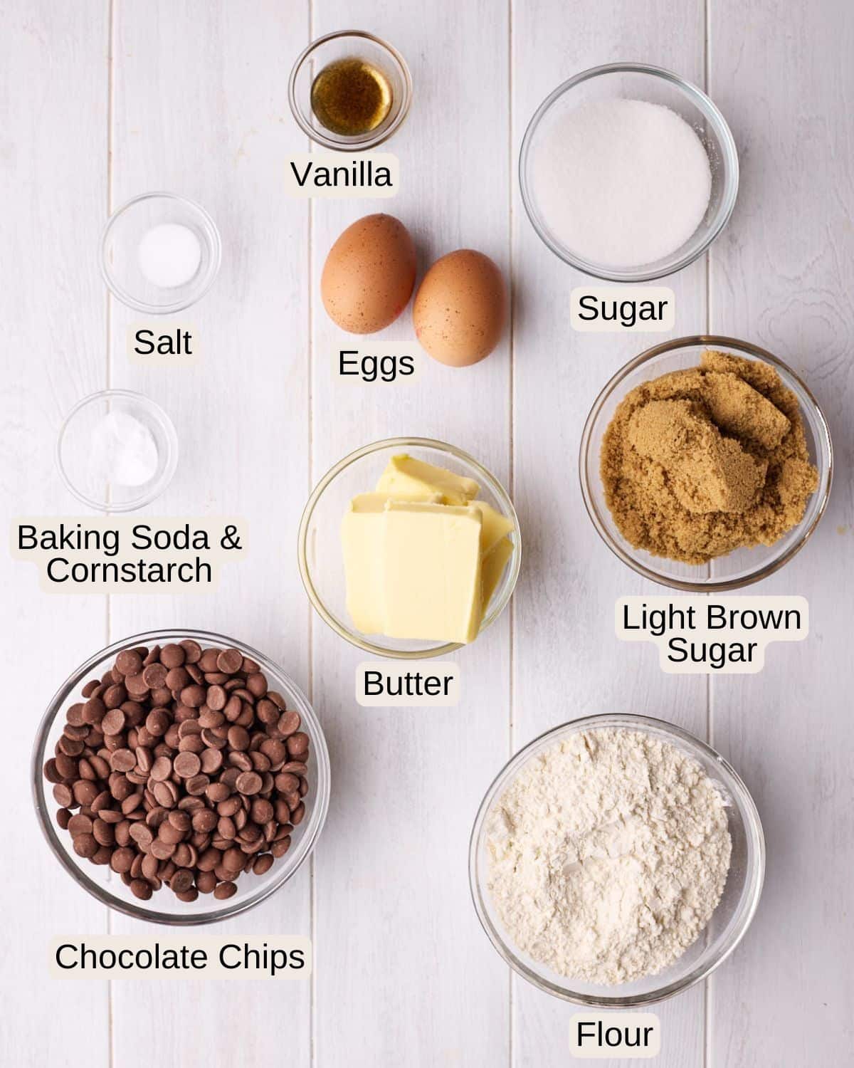 Labelled ingredients for chocolate chip cookies, including vanilla, sugar, eggs, salt, butter, light brown sugar, baking soda, cornstarch, chocolate chips, and flour.