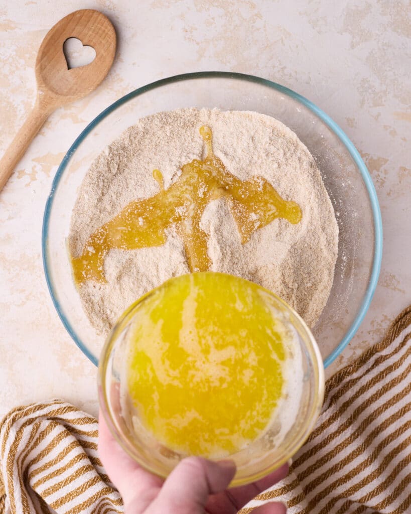 Melted butter being poured into the bowl of dry ingredients for crumb topping.