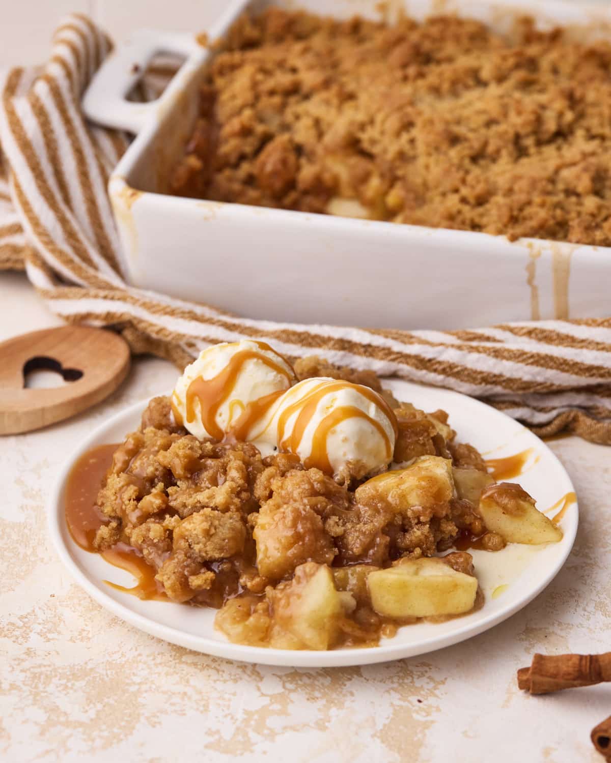 A portion of apple crumble on a plate dressed with 2 scoops of vanilla ice cream and a drizzle of caramel.