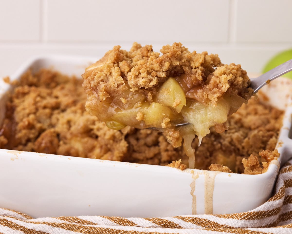 A portion of freshly baked apple crumble being scooped out of the baking dish.