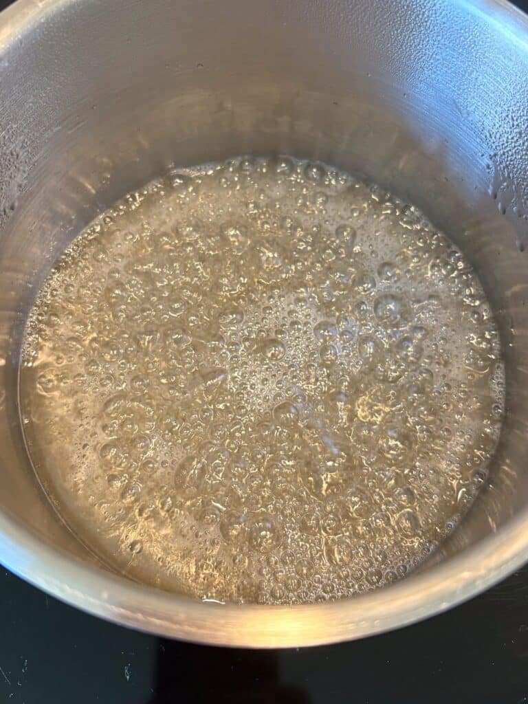 Simple syrup bubbling gently in a saucepan, looking clear.