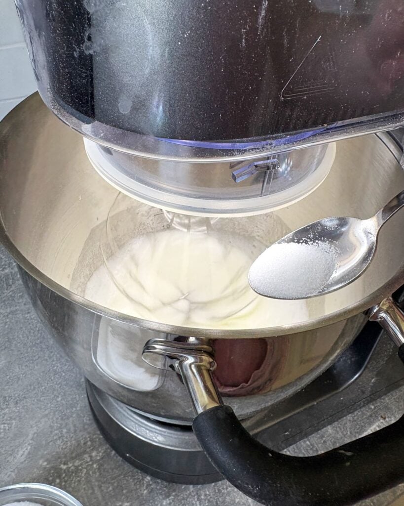 Sugar gradually being added into the whipped eggs with a spoon.