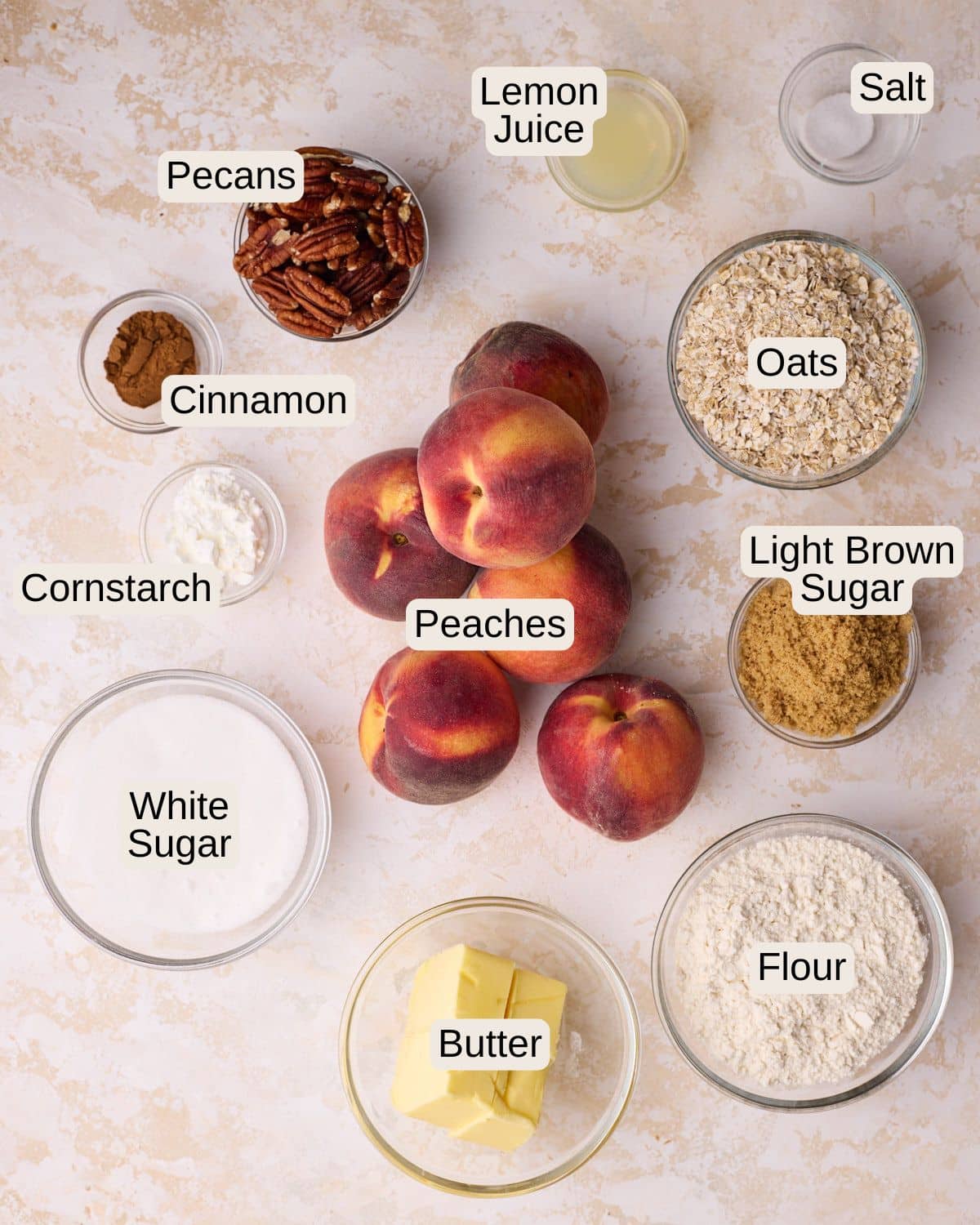 Ingredients to make peach crisp, including fresh peaches, butter, flour, white sugar, light brown sugar, oats, cinnamon, salt, lemon juice and pecans.