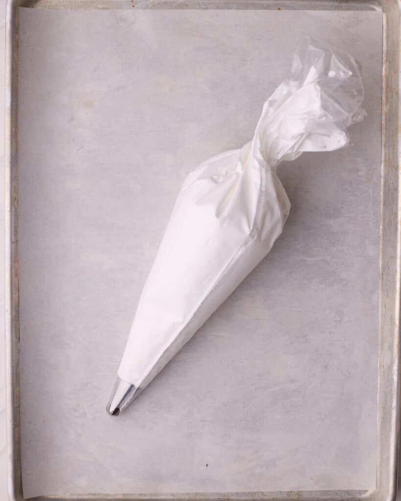 Piping bag full of meringue mixture, ready to be piped onto the prepared baking sheet.
