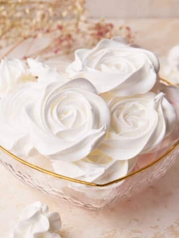White rose meringue cookies in a love heart shaped glass bowl, showing off the beautiful designs.