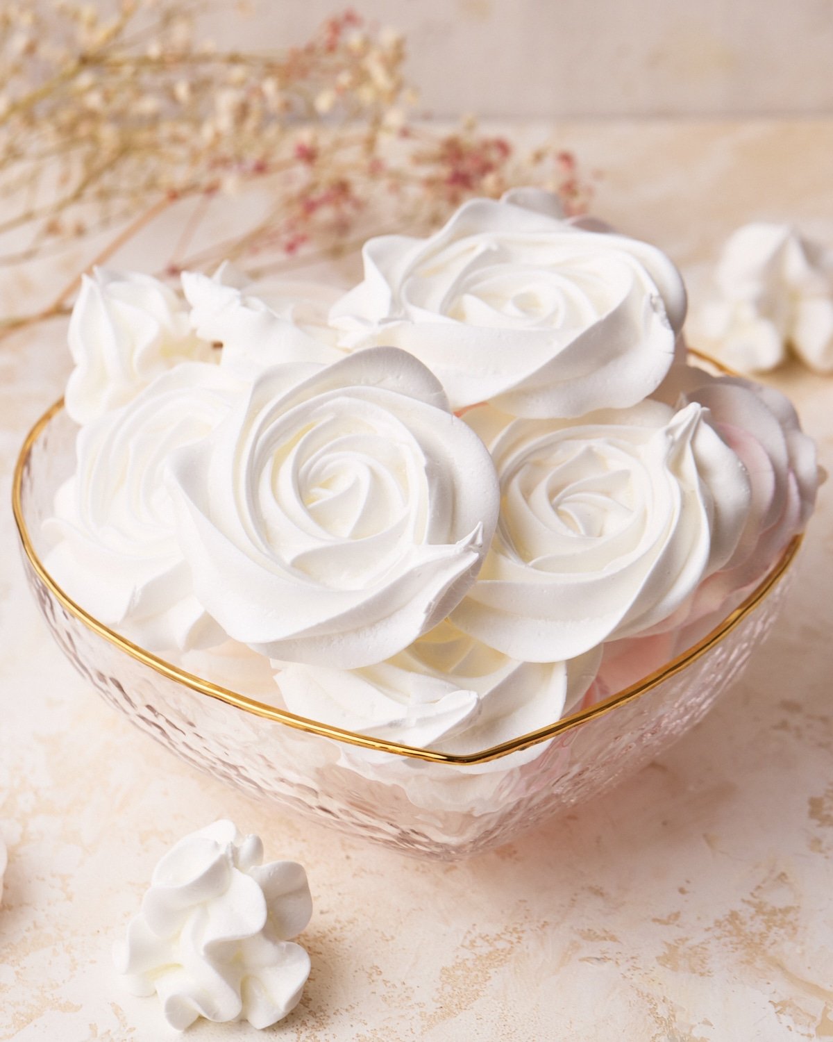 White rose meringue cookies in a love heart shaped glass bowl, showing off the beautiful designs.
