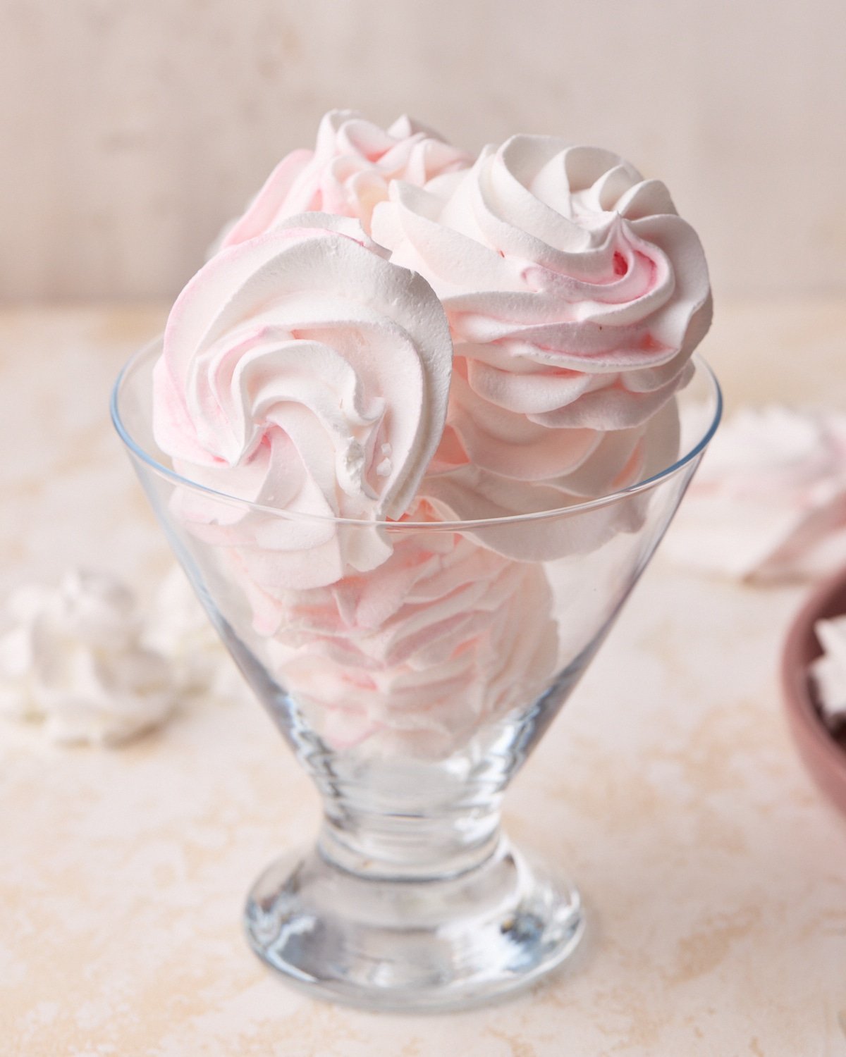 Pink and white meringue cookies shaped as roses in an individual glass dessert dish.