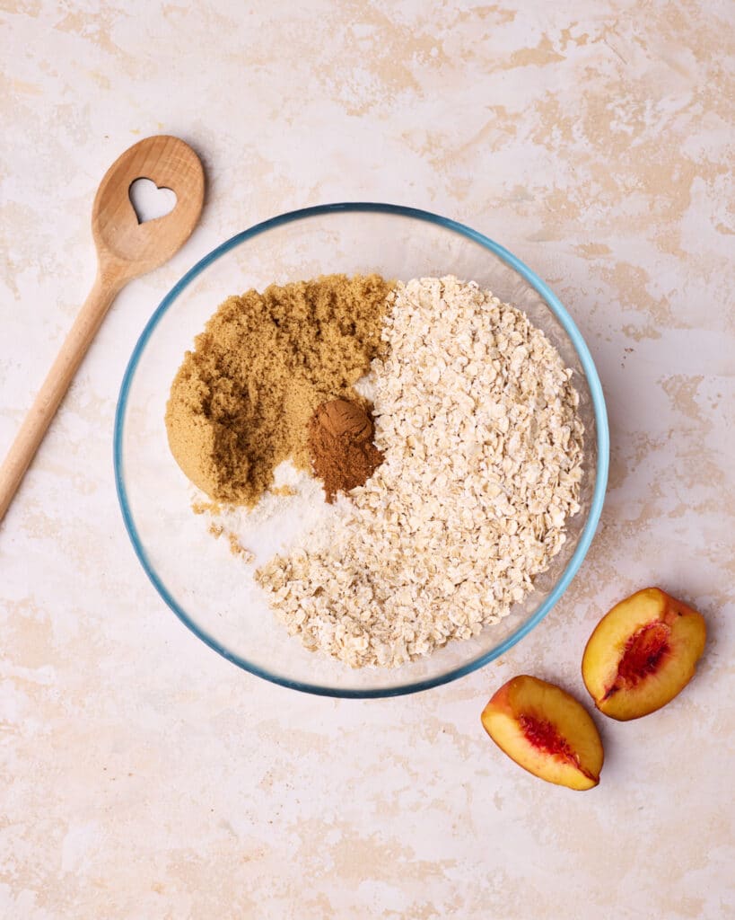 Dry ingredients to make crisp topping for peach crisp in a glass bowl, including flour, white sugar, brown sugar, cinnamon and salt. 