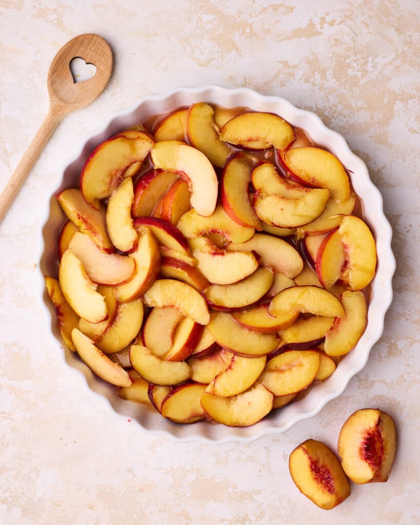 Sliced peaches coated in sugar, flour, cinnamon and lemon juice, laid out in a layer in a round pie dish. 