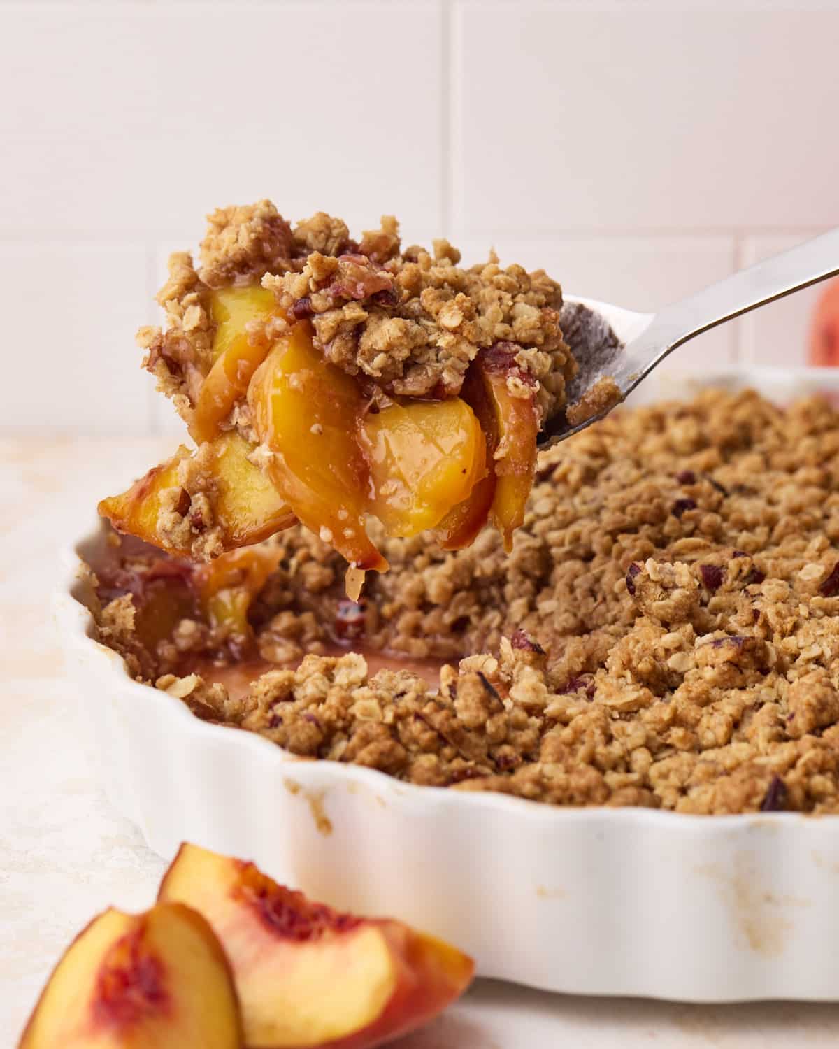 A spoonful of peach crisp being scooped out of a dish to show the soft, yellow peaches and crunchy topping.