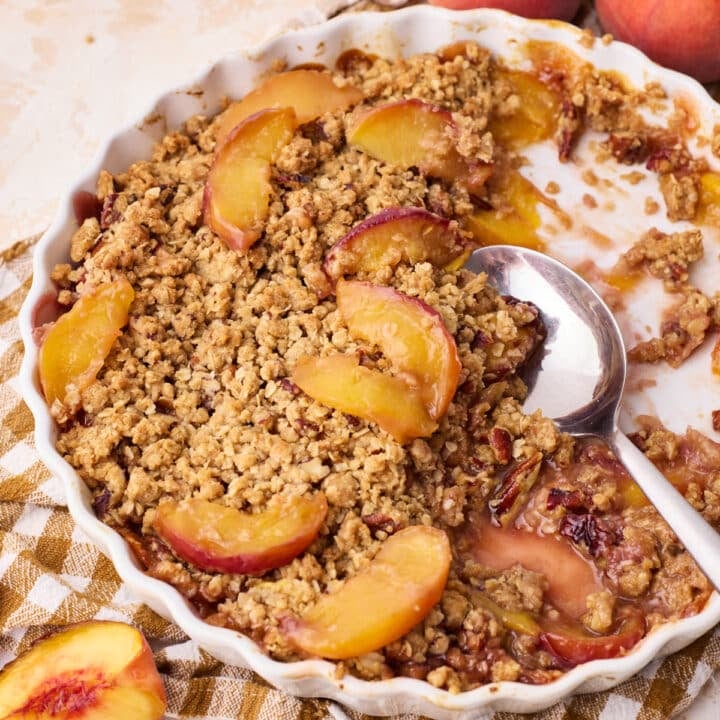 Peach crisp in a round baking dish, with half of it scooped out revealing the soft peaches underneath.