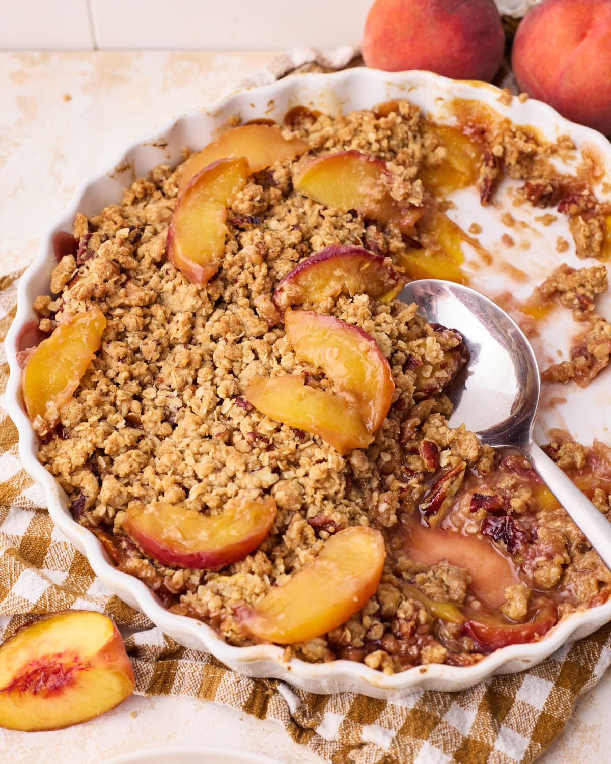 Peach crisp in a round baking dish, with half of it scooped out revealing the soft peaches underneath.
