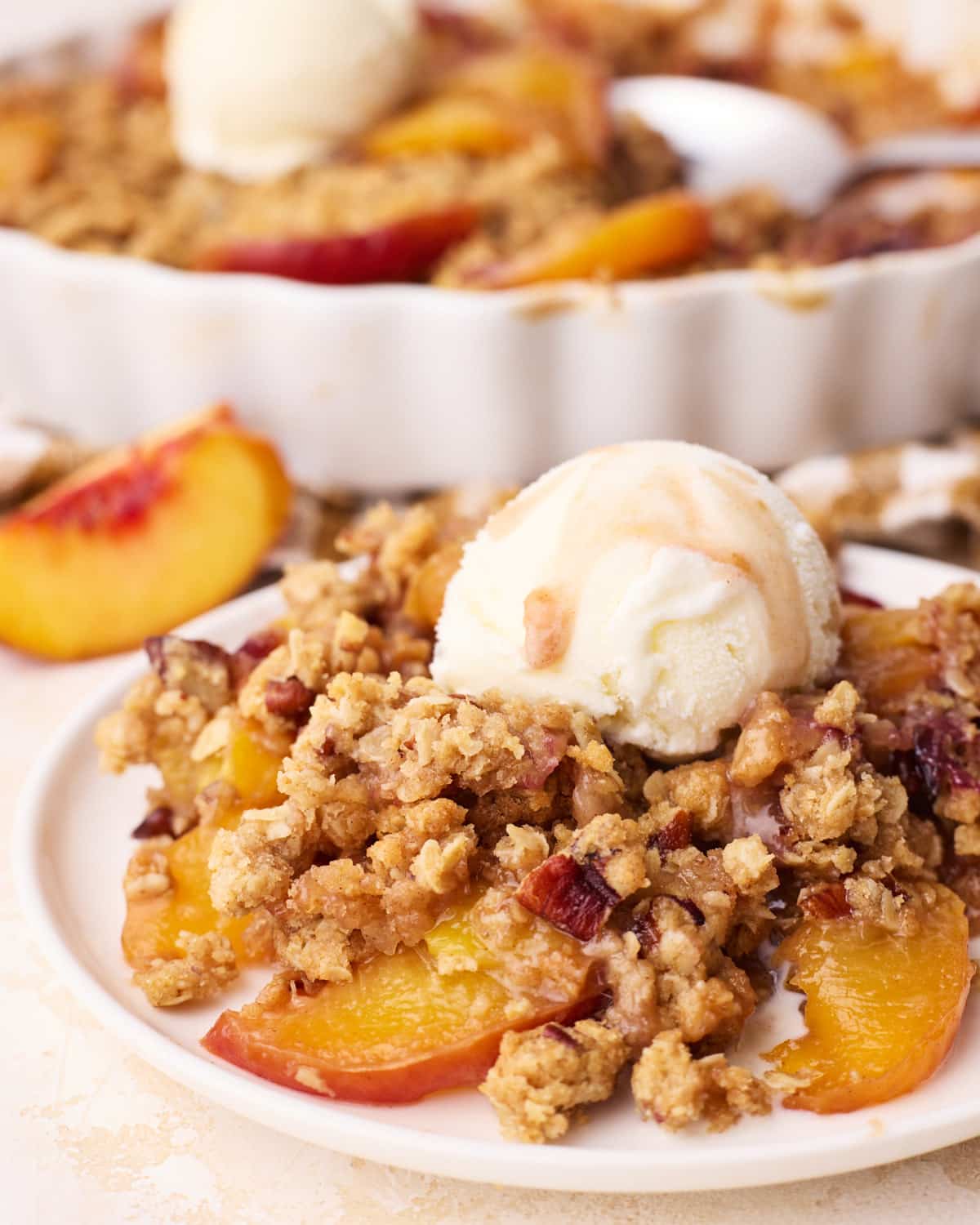 A portion of homemade peach crisp on a plate with a scoop of vanilla ice cream on top.