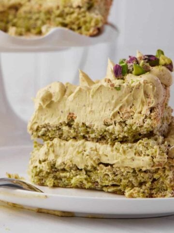 Slice of pistachio dacquoise on a plate showing crunchy dacquoise and pistachio french buttercream filling.