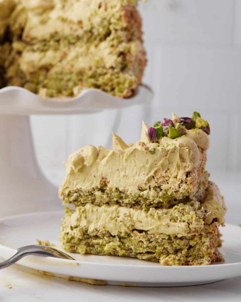Slice of pistachio dacquoise on a plate showing crunchy dacquoise and pistachio french buttercream filling.