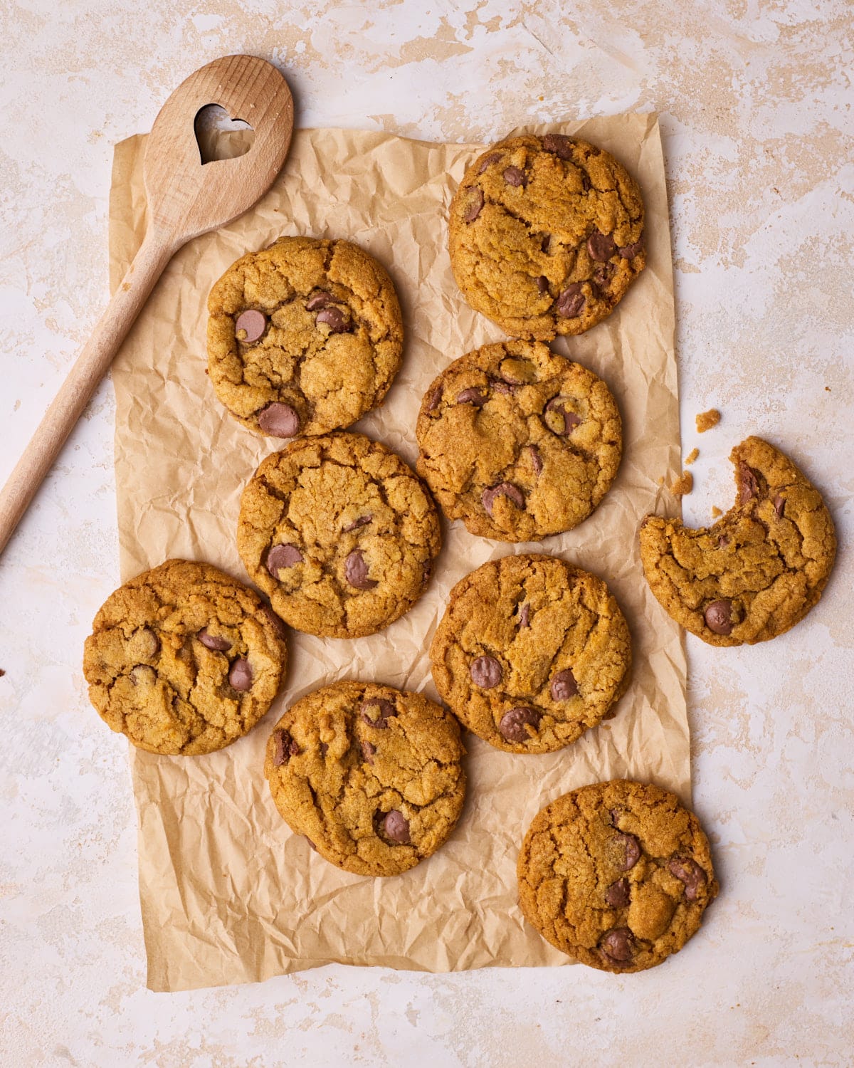 Freshly baked pumpkin chocolate chip cookies on a piece of parchment paper, with a bite taken out of one.