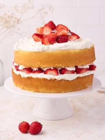 Vanilla sponge cake filled with strawberries and cream, on a white cake stand.