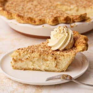 Side view of a slice of coconut custard pie on a plate with the rest of the pie in the background.