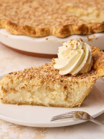 Side view of a slice of coconut custard pie on a plate with the rest of the pie in the background.