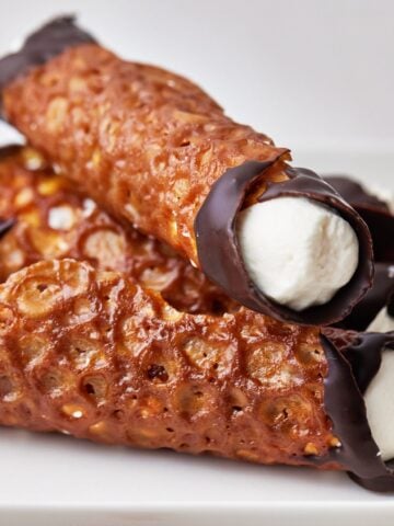 Brandy snap lace cookies in a pile, dipped in chocolate and filled with cream.