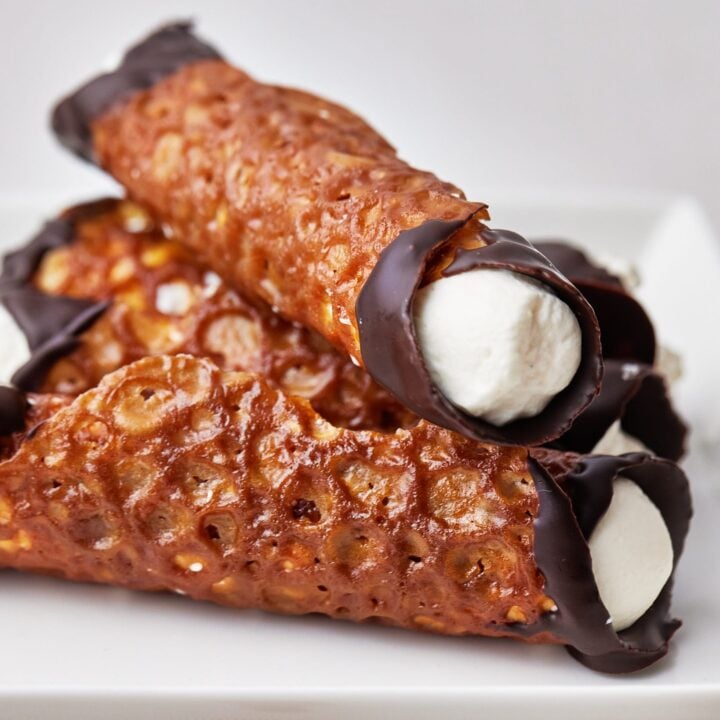 Brandy snap lace cookies in a pile, dipped in chocolate and filled with cream.