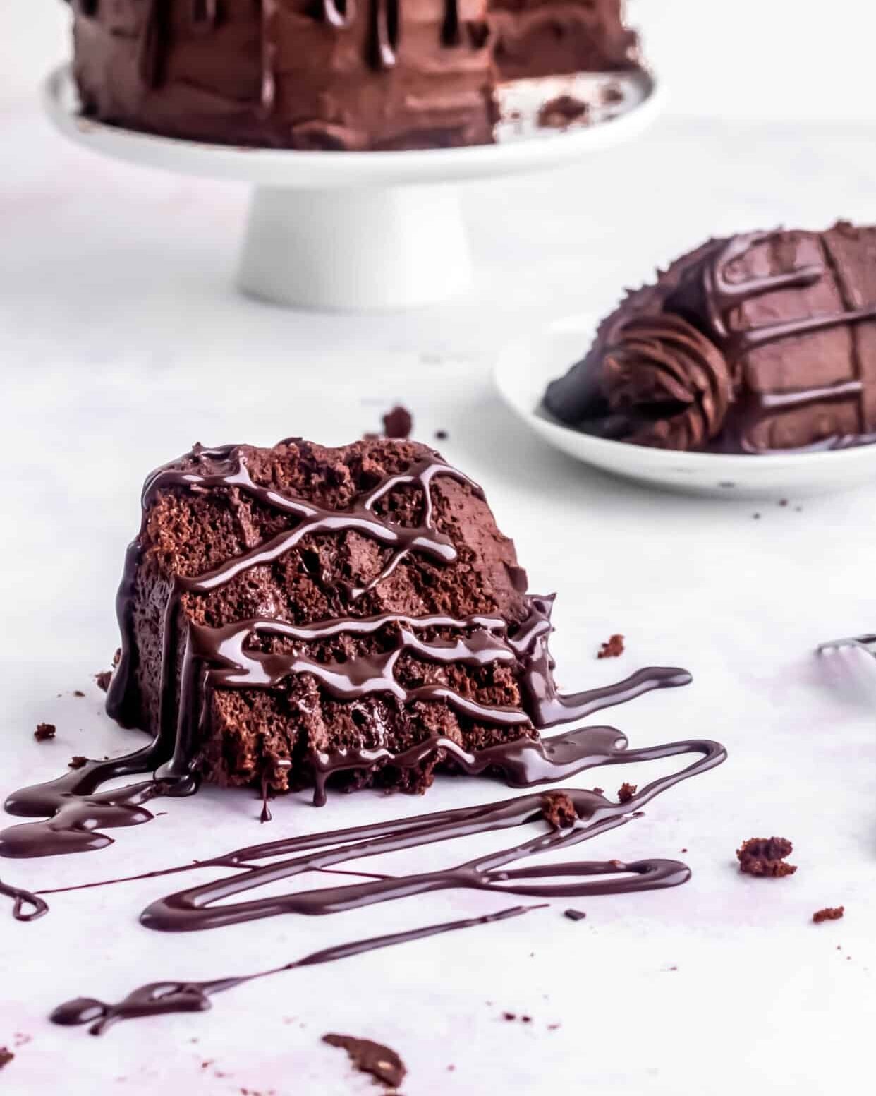 Slice of chocolate cake with chocolate ganache drizzled all over it and the table. 