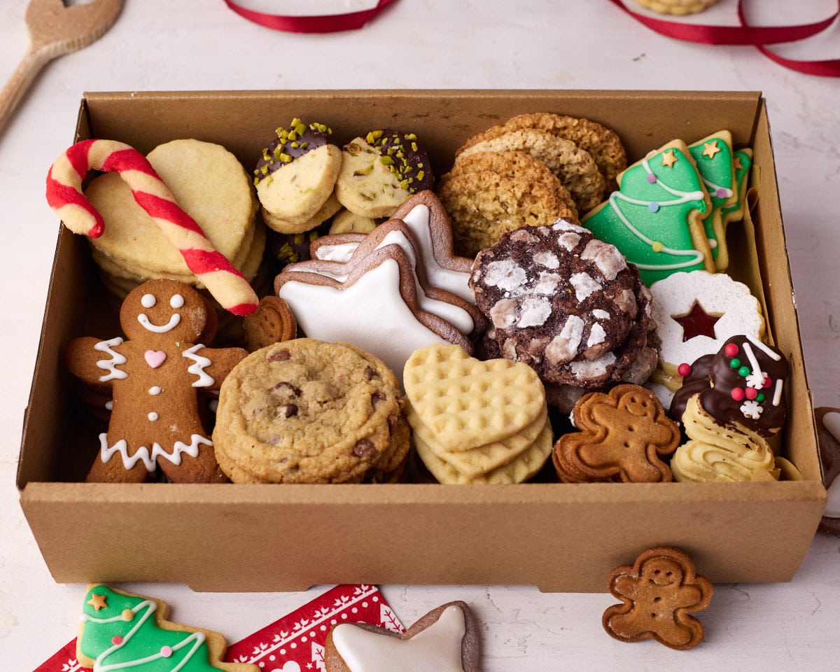 An open cookie box displaying all of the different cookies, with festive decorations and spare cookies dotted around the outside.